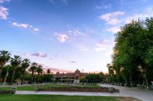 View of blue sky and UArizona Old Main building and green grassy area